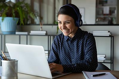 蓝衣女学生坐在笔记本电脑前的桌子旁，对着电脑微笑